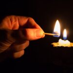 person holding match stick with fire in front of candle with fire